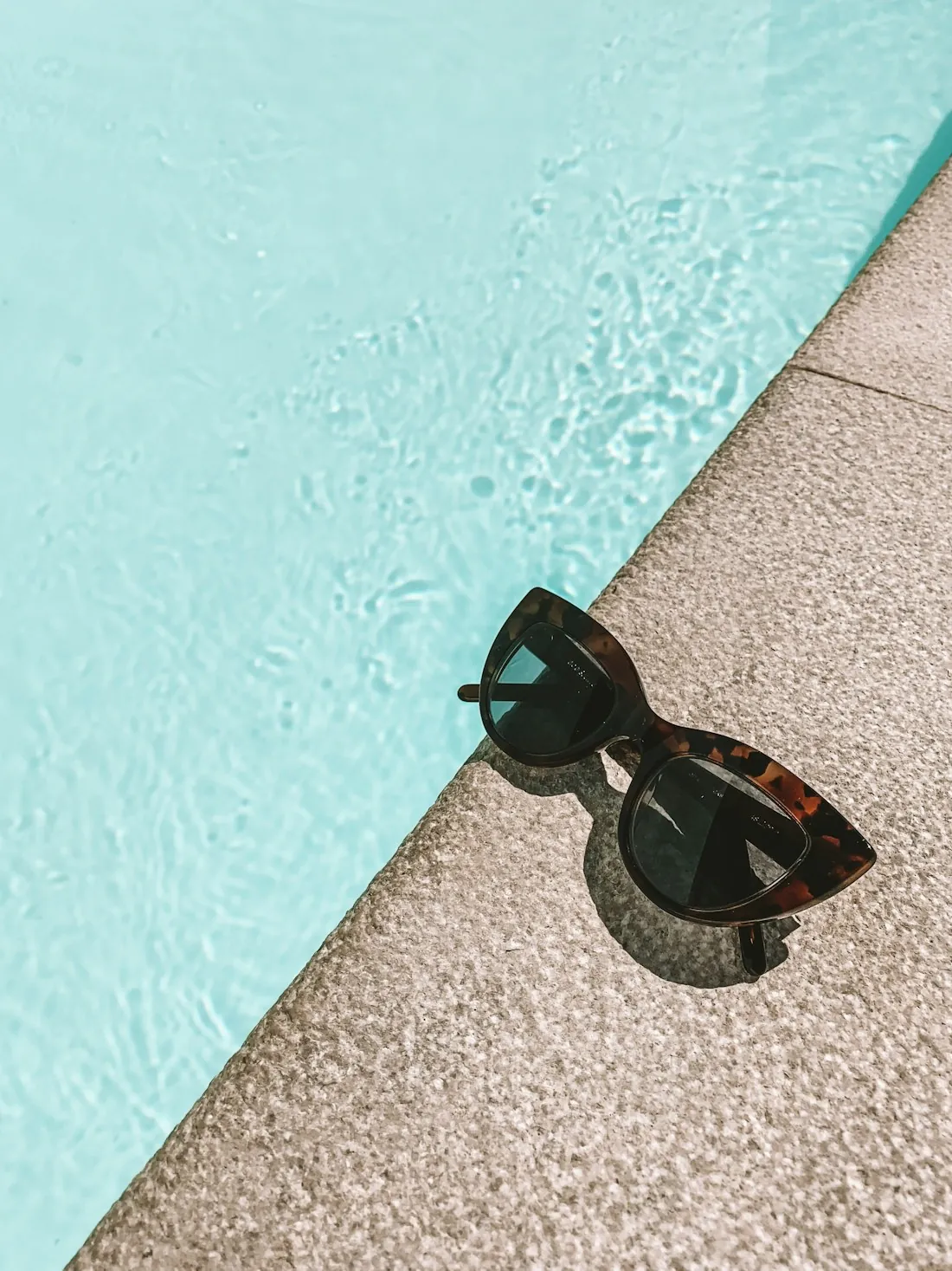 Sunglasses resting beside a swimming pool